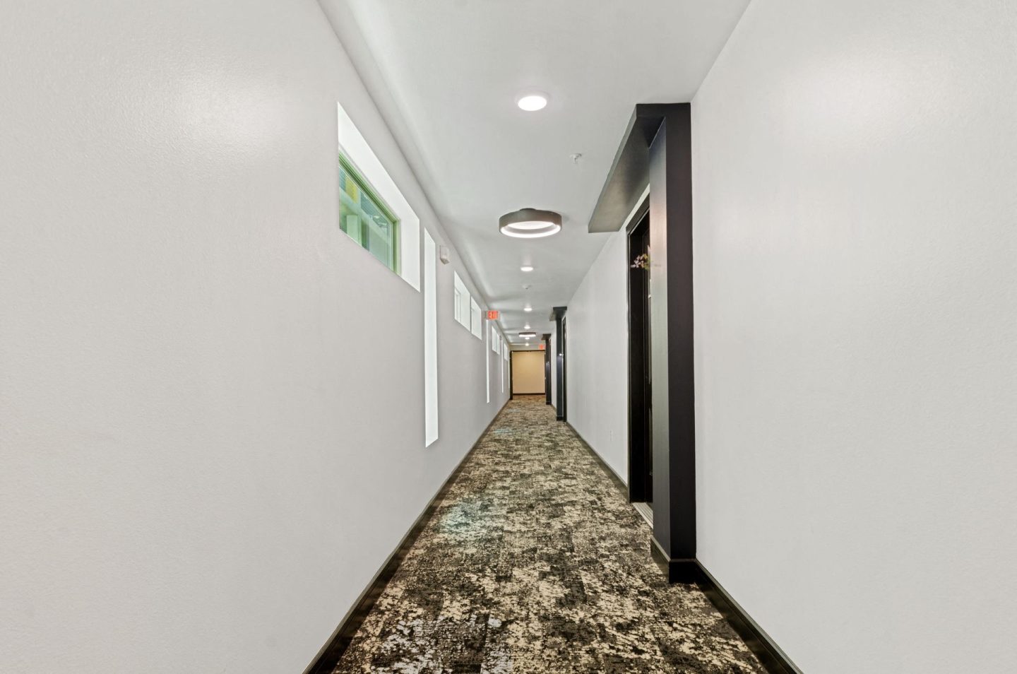 a long corridor with white walls and black doors and carpeted floors