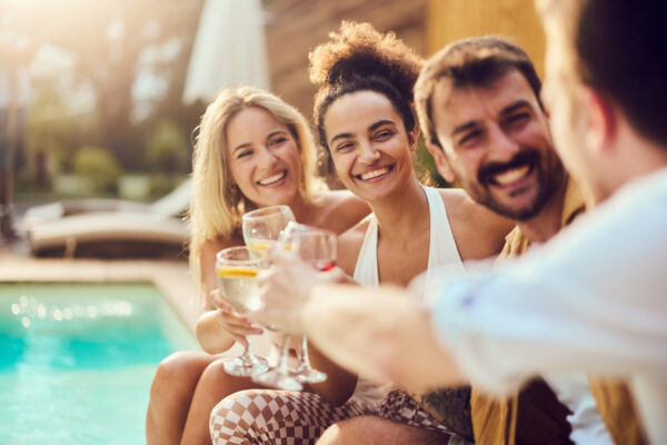 Group of happy friends having fun while toasting with drinks in summer day by the pool.