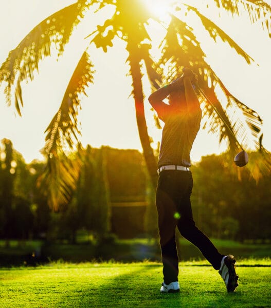 asian man playing golf on a golf course against sunset