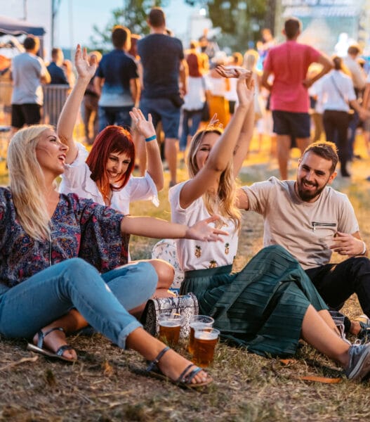 Group Of People Sitting On A Grass And Dancing At The Music Festival
