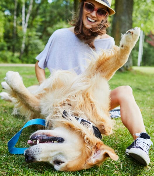 Joyful young woman playing with her dog outdoors in the park