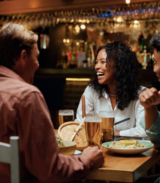 Young multiracial group of friends in casual clothing laughing around table with food and drinks