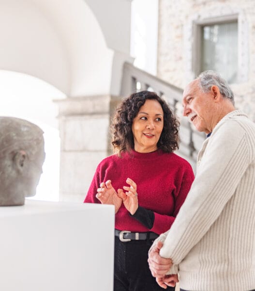 Adult Woman Discussing The Statue With A Senior Caucasian Male In A History Museum