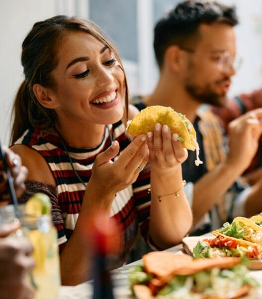Happy woman eating tacos during a lunch with friends in Mexican restaurant.