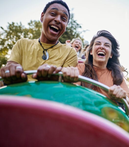 Cheerful couple having fun while riding on rollercoaster at amusement park.