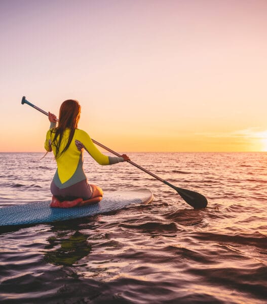 Girl on stand up paddle board, quiet sea with warm sunset colors. Relaxing on ocean